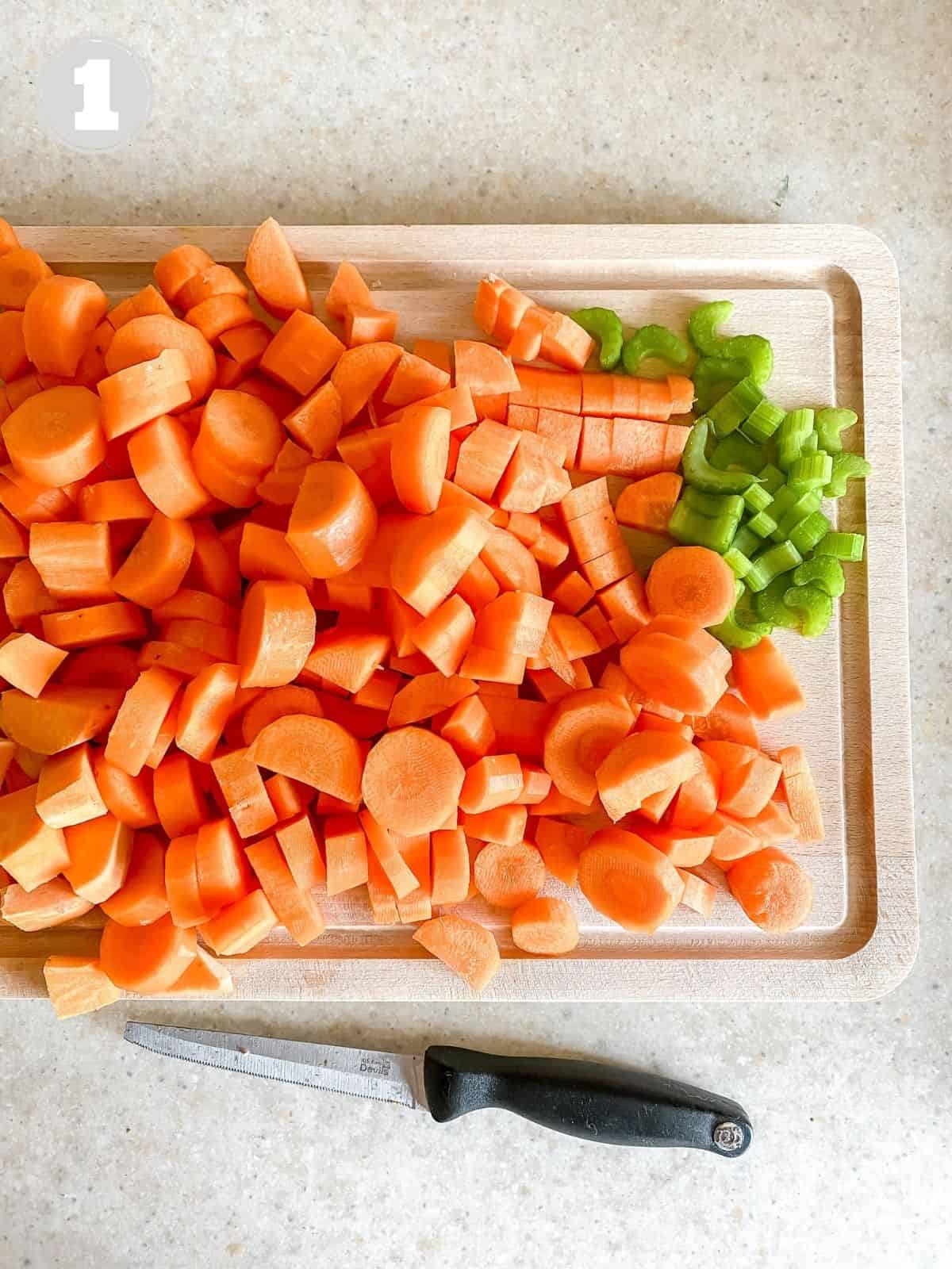 carrot and celery on a wooden chopping board next to a knife.