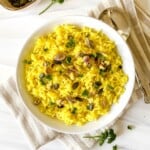 coconut turmeric rice in a white bowl on a white and beige striped cloth next to a spoon.
