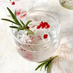 elderflower fizz mocktail in a glass with pomegranate seeds and rosemary.