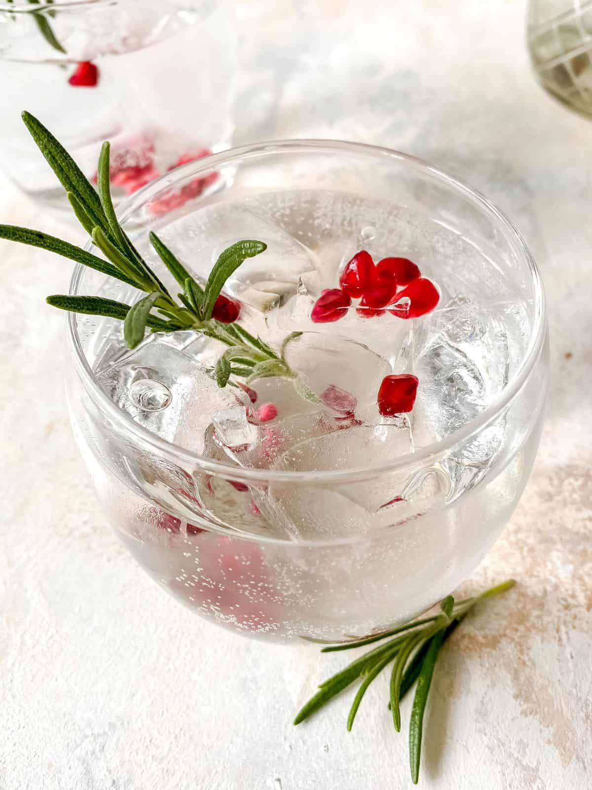 elderflower fizz mocktail in a glass with pomegranate seeds and rosemary.