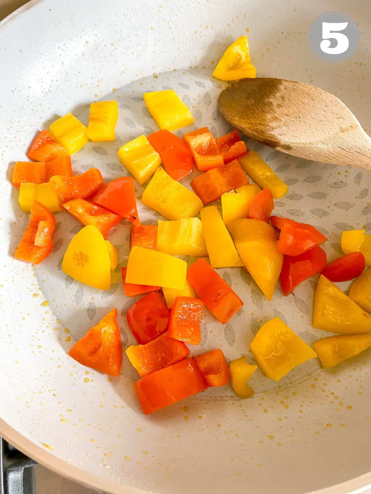 yellow and red diced bell pepper in skillet with a wooden spoon stirring them labelled number five.