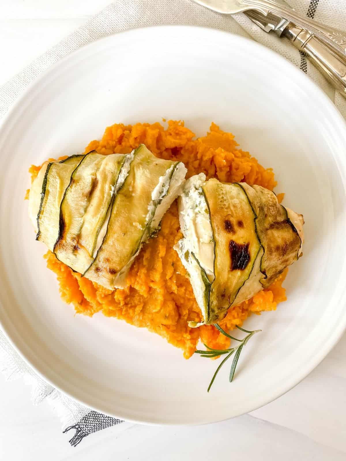two pieces of cream cheese stuffed chicken on a bed of sweet potato mash on a white plate.