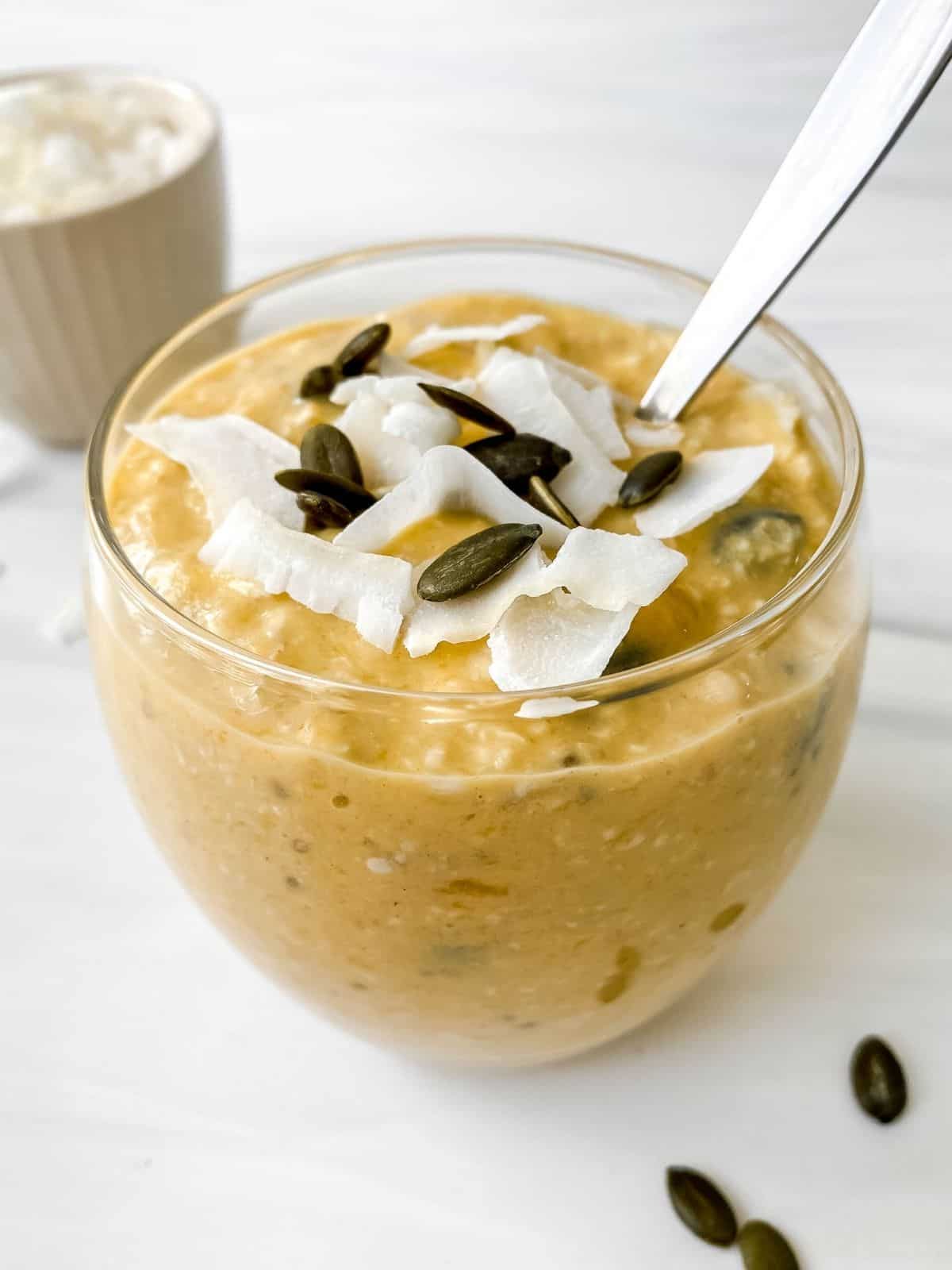 mango coconut overnight oats in a glass jar with a bowl of coconut in the background.