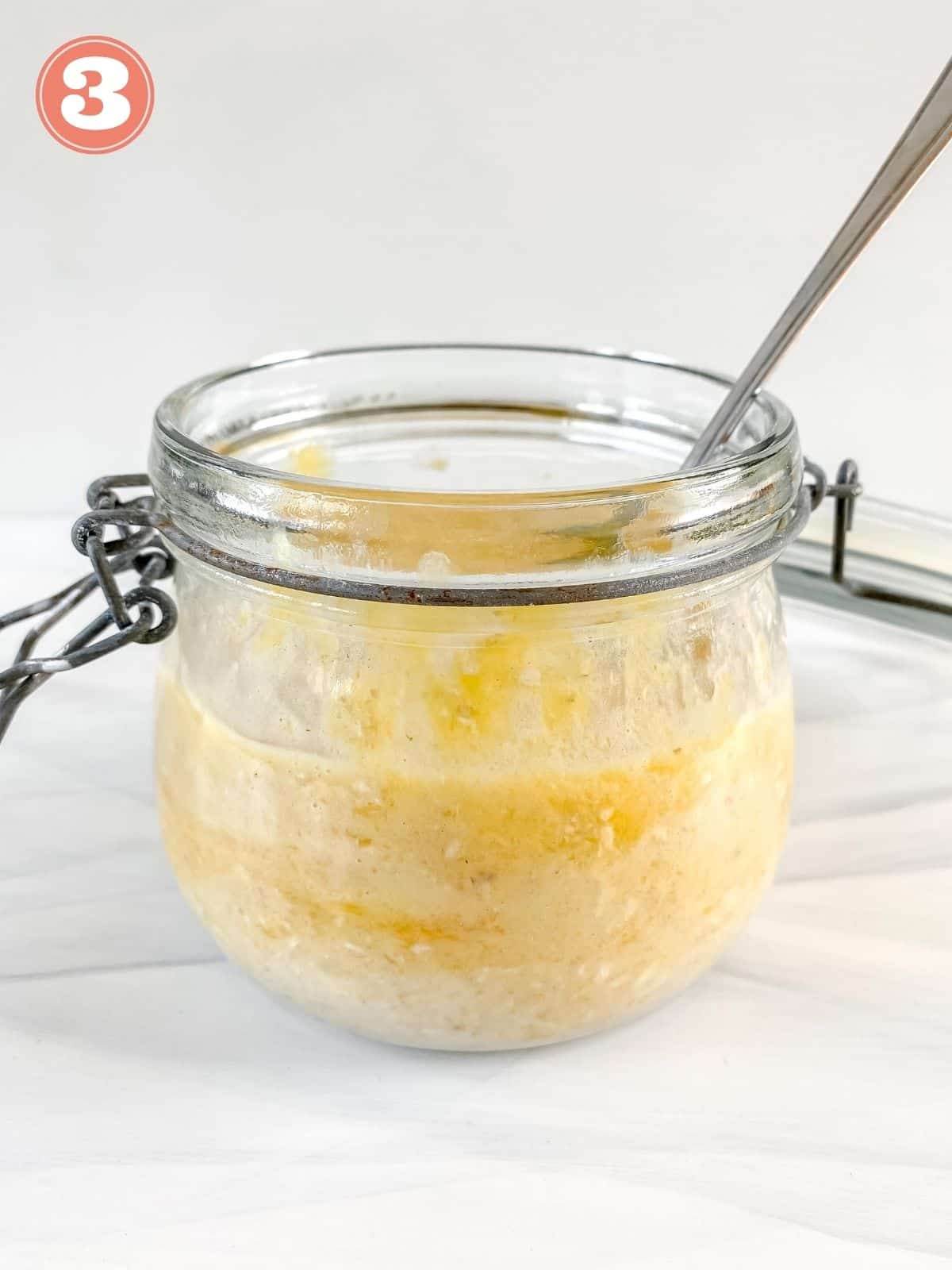 oats, milk and mango in a glass jar with a spoon in it.