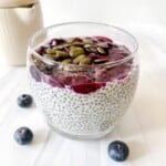 berry chia pudding in a glass jar next to blueberries and a cream jug.
