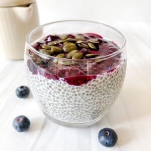 maple chia pudding with blueberry jam next to a jug and blueberries.
