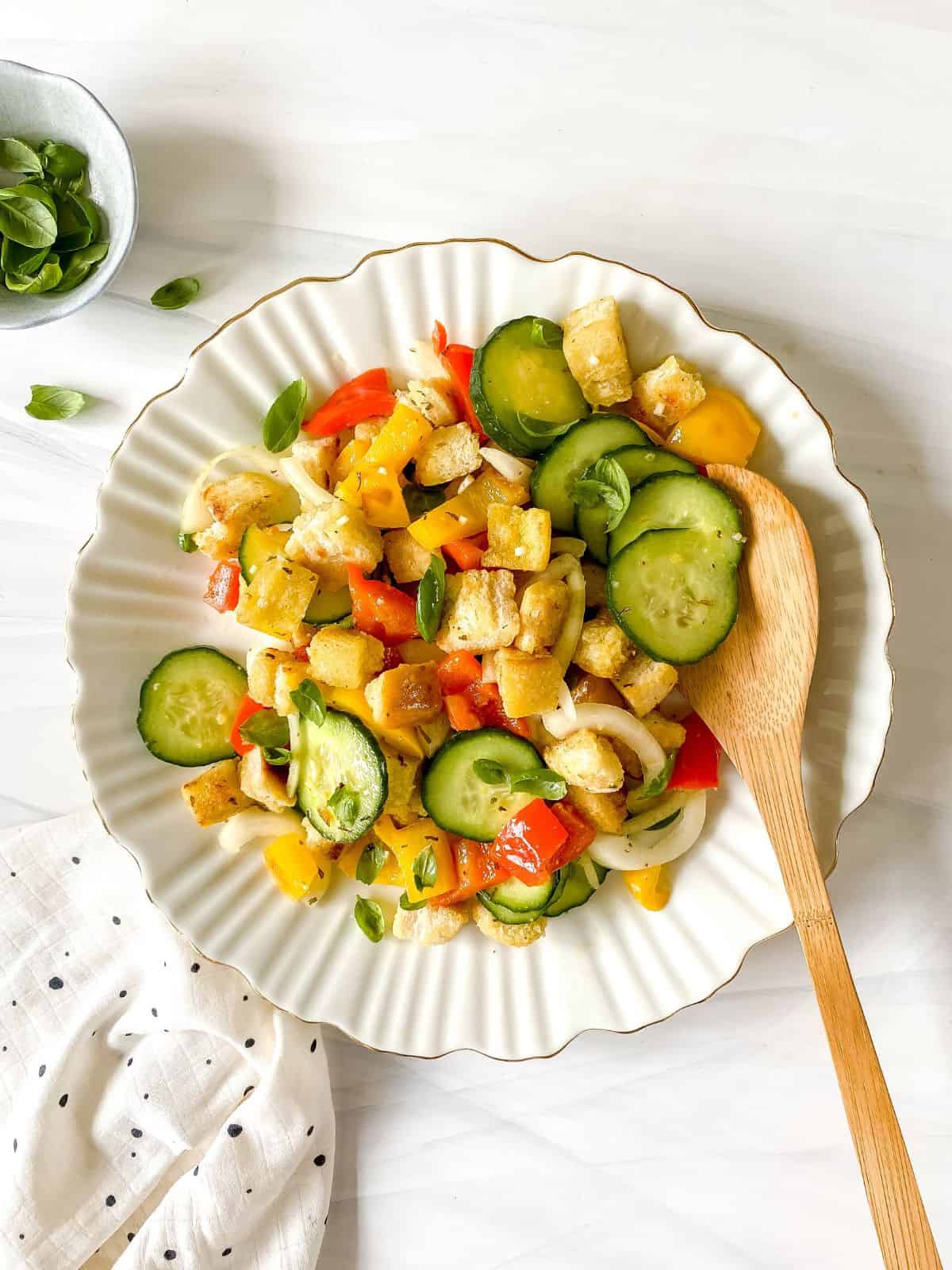 panzanella without tomatoes on a white round plate with a wooden spoon in it.