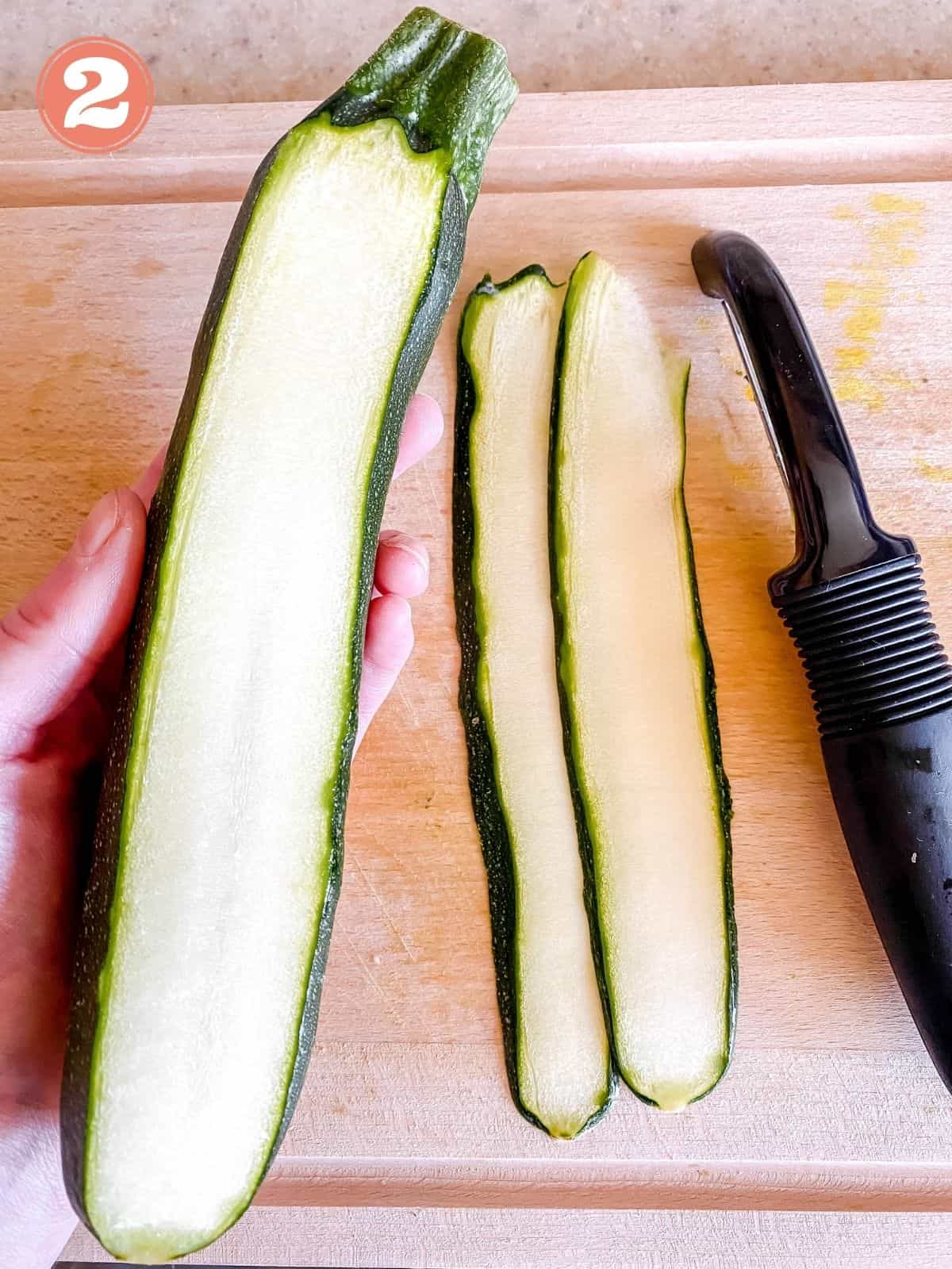 peeled zucchini and someone holding a zucchini above a wooden chopping board labelled number two.