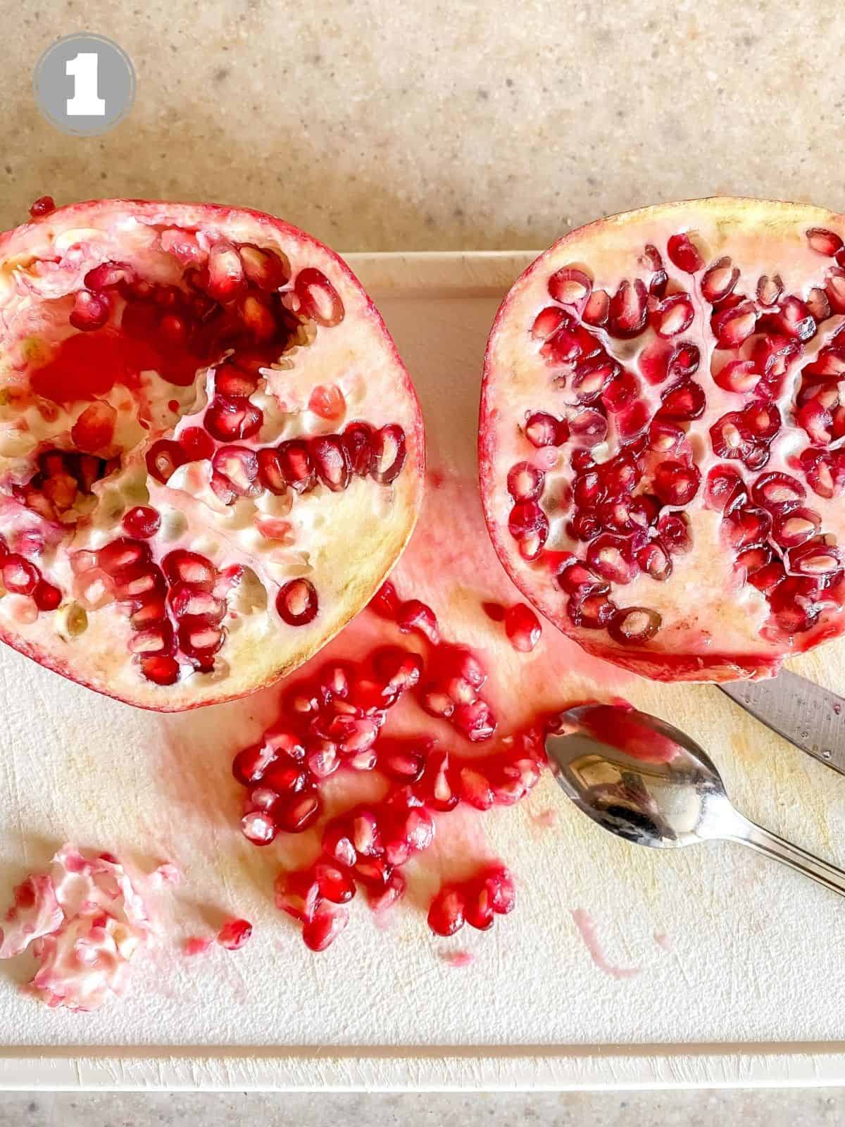 two pomegranate halves on a board with a spoon and knife.