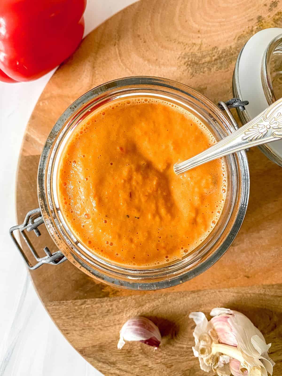 roasted red pepper nomato sauce in a glass jar with a spoon in it.