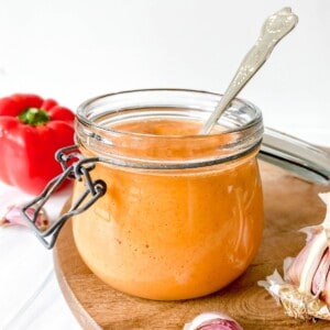 roasted red pepper nomato sauce in a glass jar with a spoon in it.