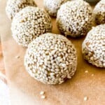 sesame energy balls on a lined wooden board next to a bowl of sesame seeds.