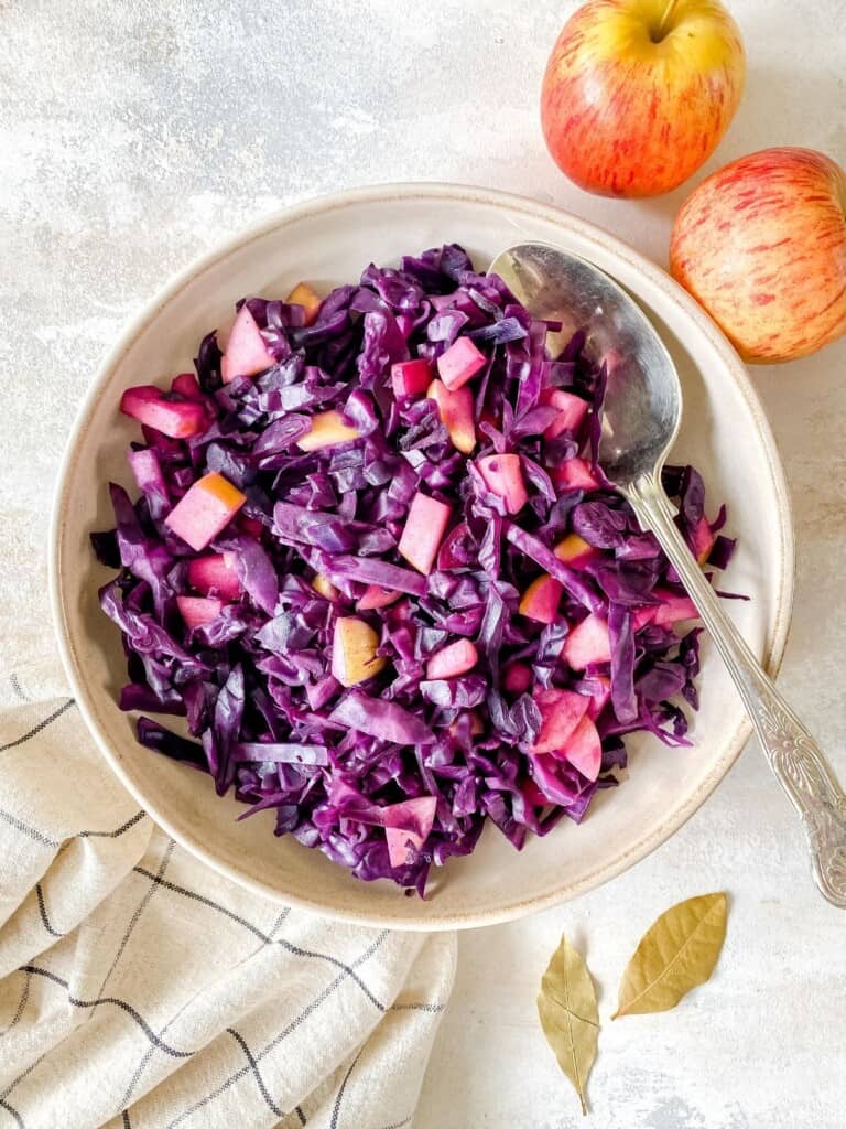 vegan braised red cabbage with apple in a light brown bowl with a spoon in it.