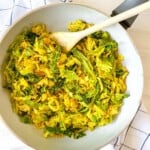 vegan fried cabbage in a white pan with a wooden spoon in it.