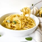 vegan pumpkin pasta in a white dish with a fork lifting pasta out.