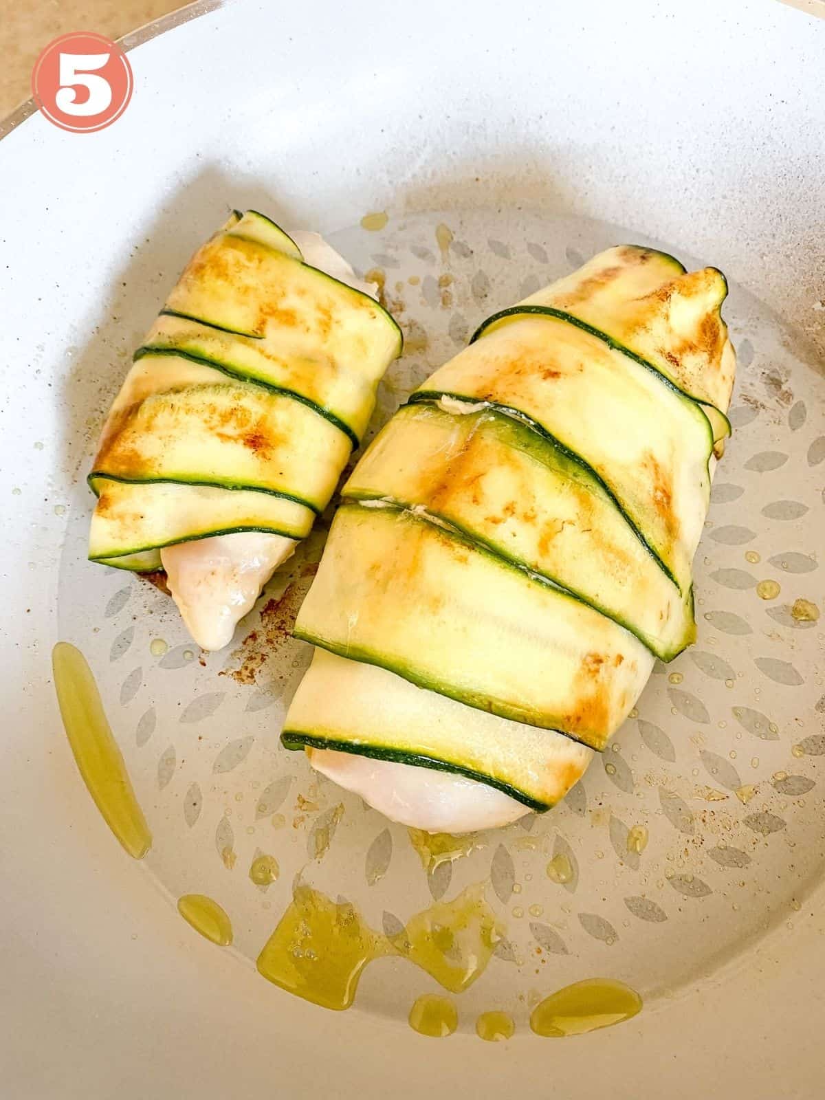 zucchini wrapped chicken breasts in a skillet.