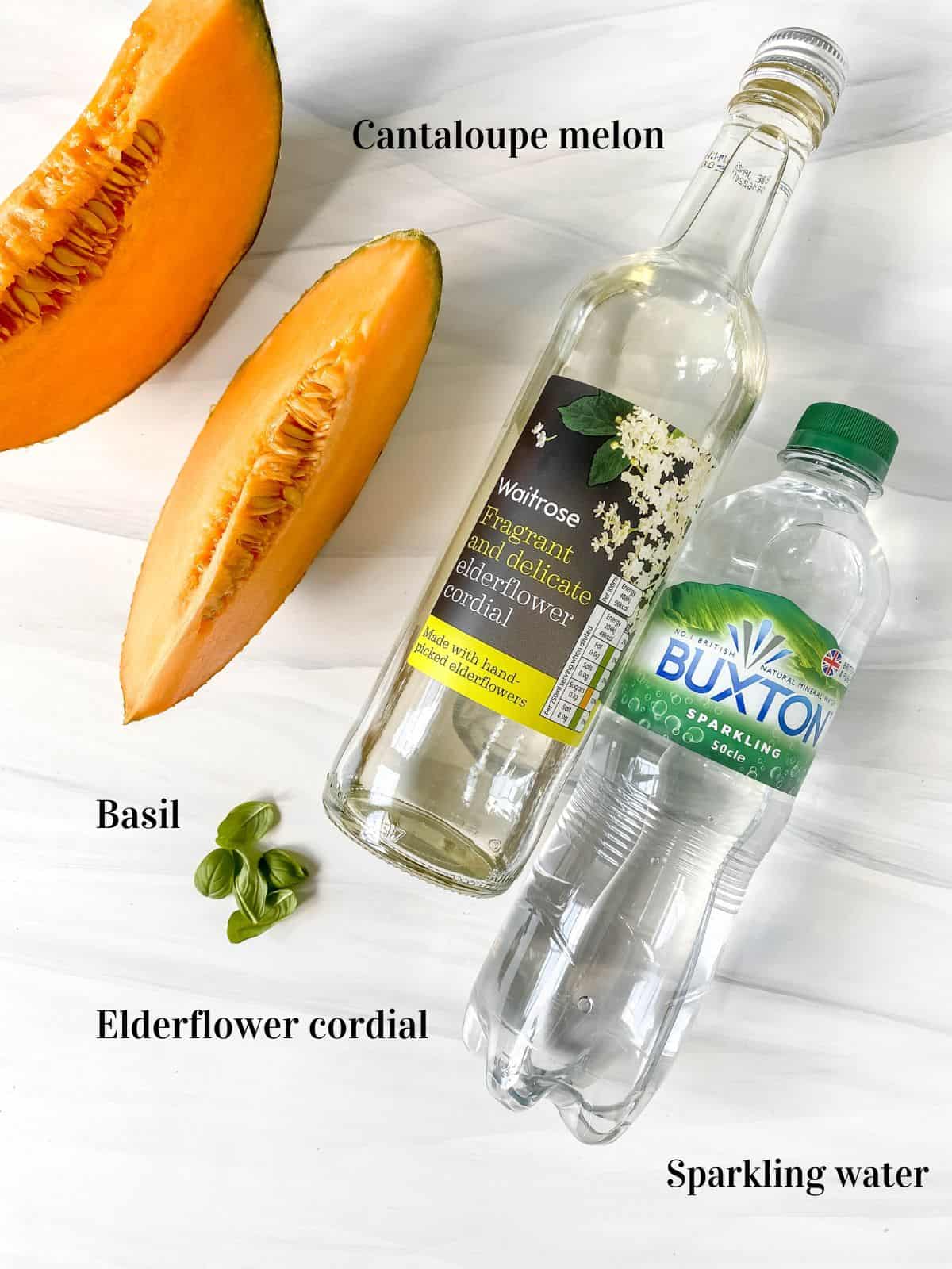 labelled ingredients to make cantaloupe mocktail including sparkling water and basil.