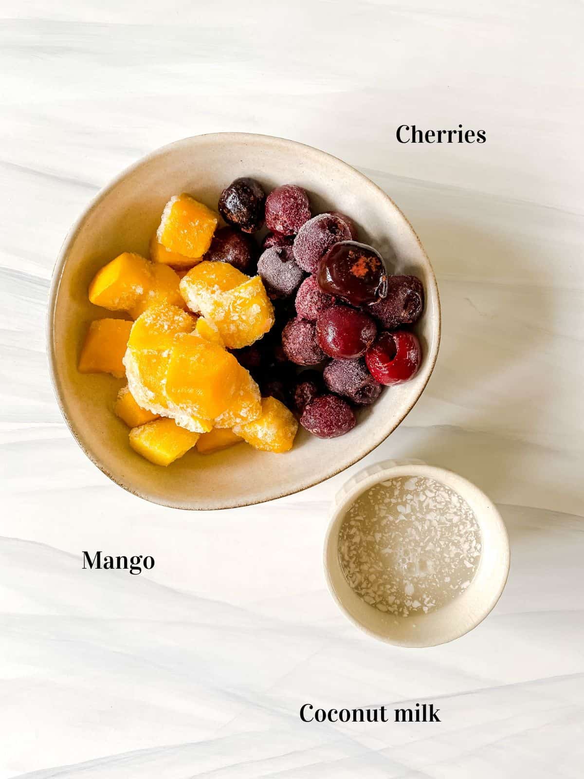 bowl of cherries and mango next to a bowl of coconut milk.