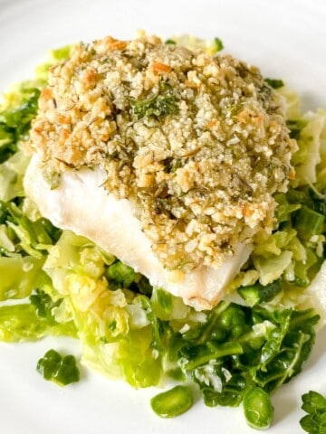 almond crusted cod on a bed of cabbage on a white plate.