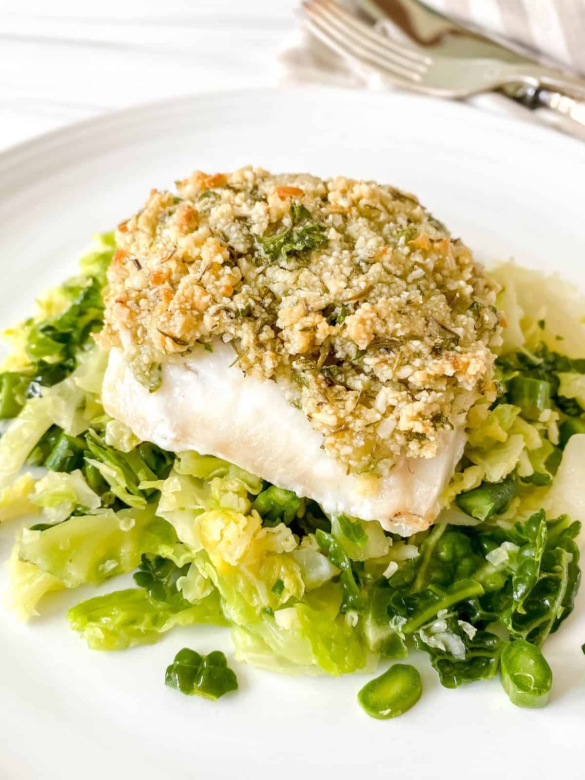 almond crusted cod on a bed of cabbage on a white plate.