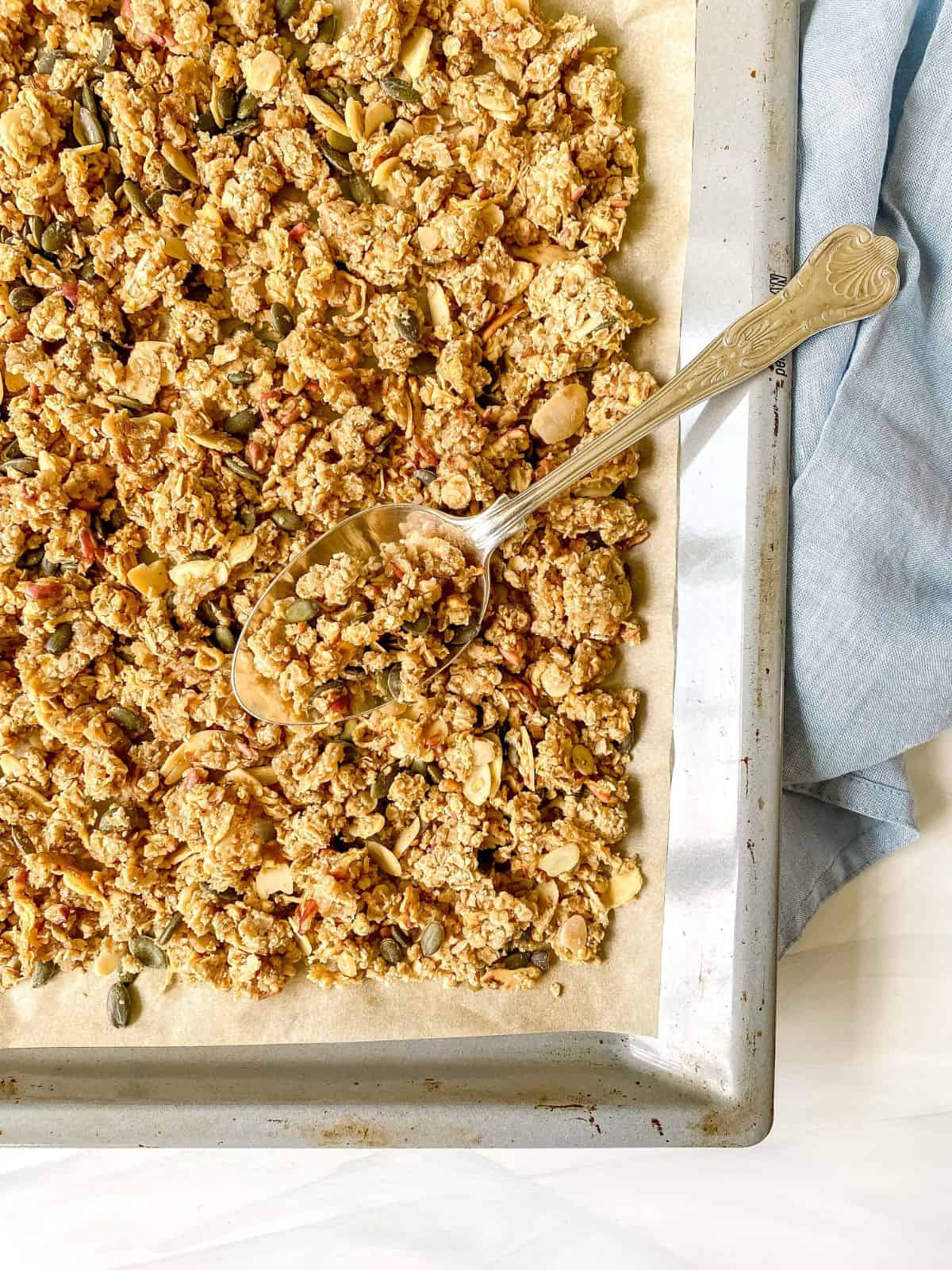 apple pie granola on a baking tray with a spoon on it.
