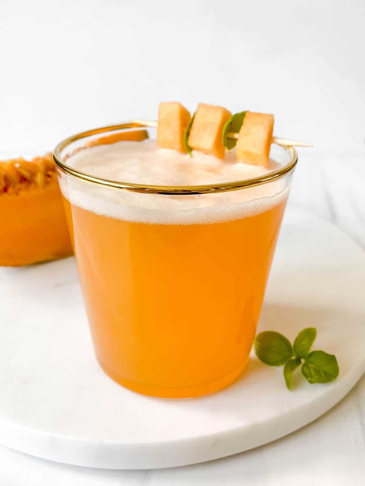 cantaloupe melon mocktail in a glass on a marble serving plate with melon in the background.