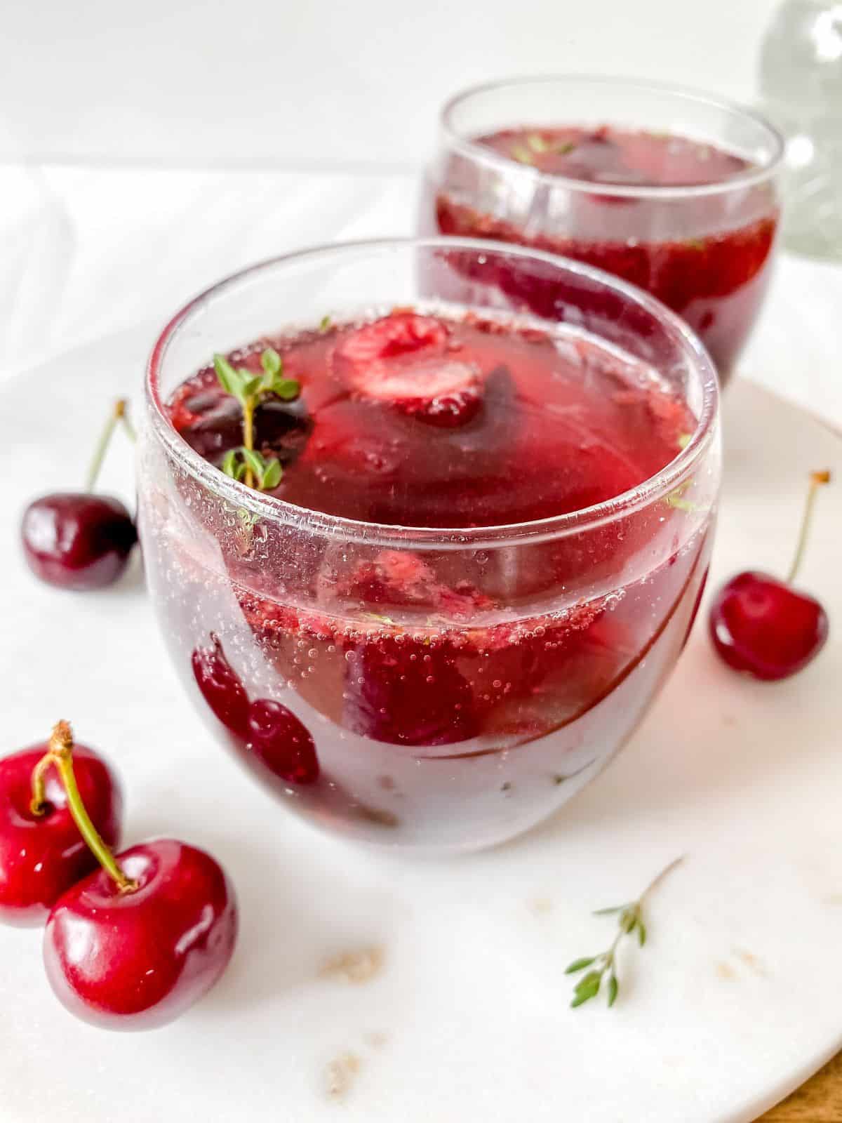 cherry mocktail in two glasses next to cherries and thyme sprigs.