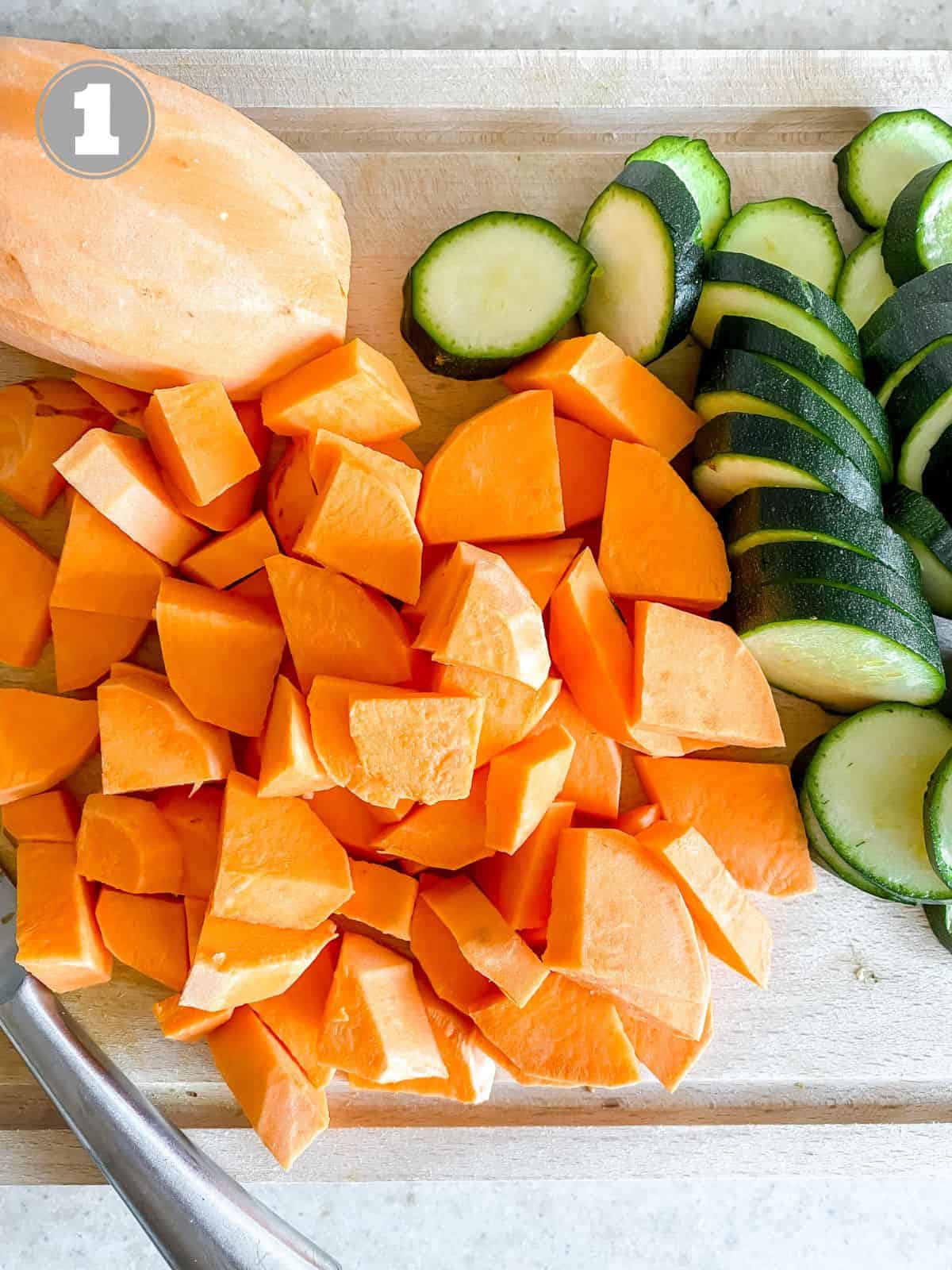 diced sweet potato and zucchini on a wooden board with a knife.