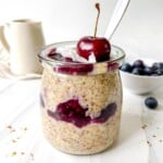 flaxseed pudding in a glass jar with a cherry on it with a jug in the background.