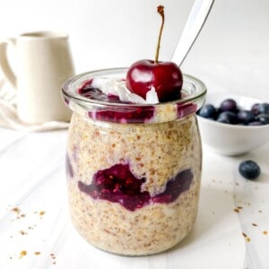 flaxseed pudding in a glass jar with a cherry on it with a jug in the background.