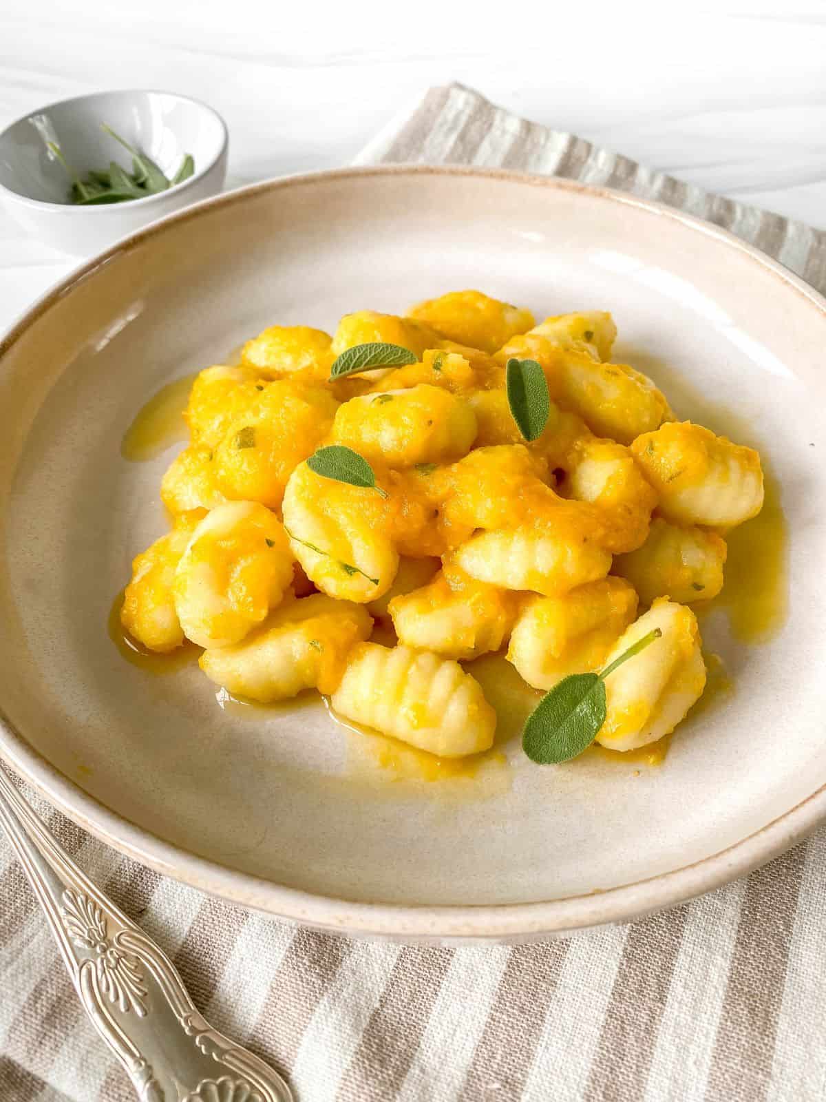 gnocchi with butternut squash sauce in a light brown bowl on a striped cloth.