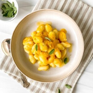 gnocchi with butternut squash sauce on a striped cloth next to a bowl of sage.