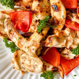 honey ginger grilled chicken on a white plate with red bell pepper and parsley.