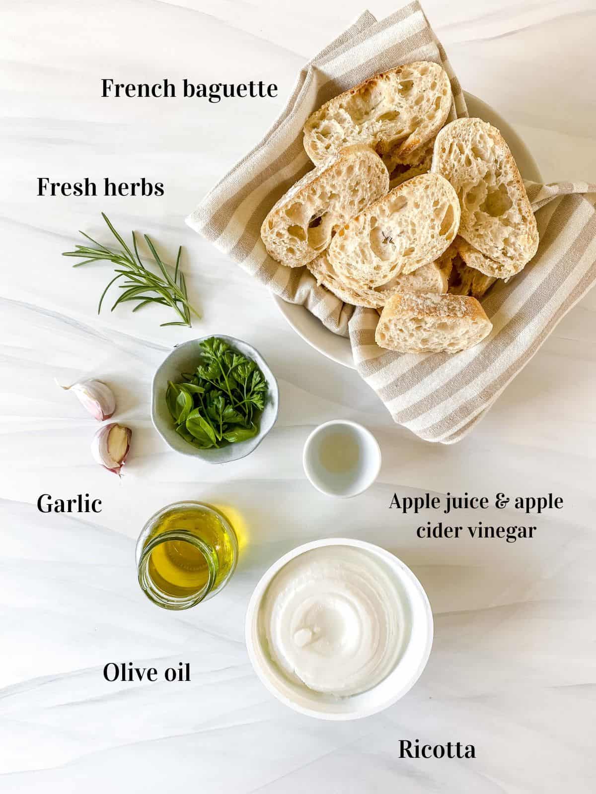 individually labelled ingredients for whipped ricotta crostini including French baguette, fresh herbs and olive oil.