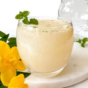 lychee mocktail in a glass with mint next to yellow flowers.
