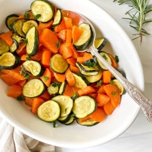 roasted sweet potatoes and zucchini in a white dish with an ornate spoon in it.