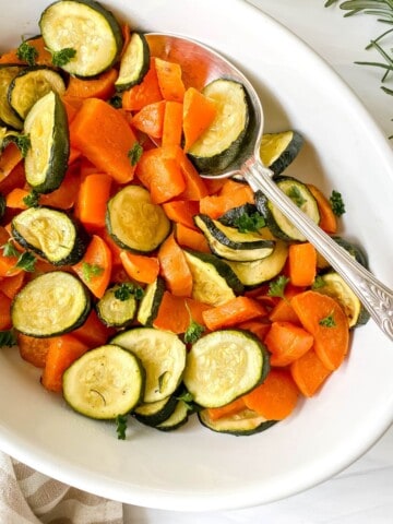 roasted sweet potatoes and zucchini in a white dish with an ornate spoon in it.
