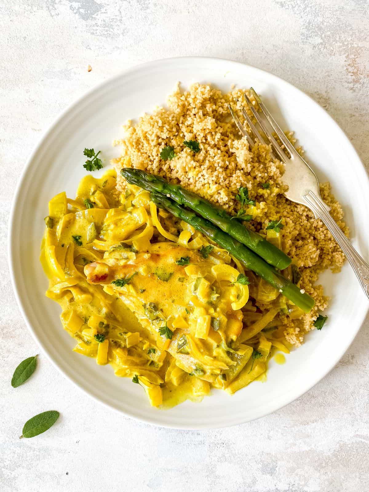turkey with sage cream sauce on a plate with couscous and asparagus and a fork.