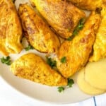 turmeric turkey breast fillets on a plate with herbs and ginger slices.