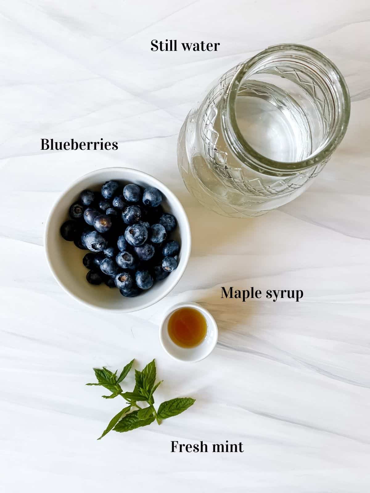 labelled bowl of blueberries, jug of water, bowl of maple syrup and fresh mint.