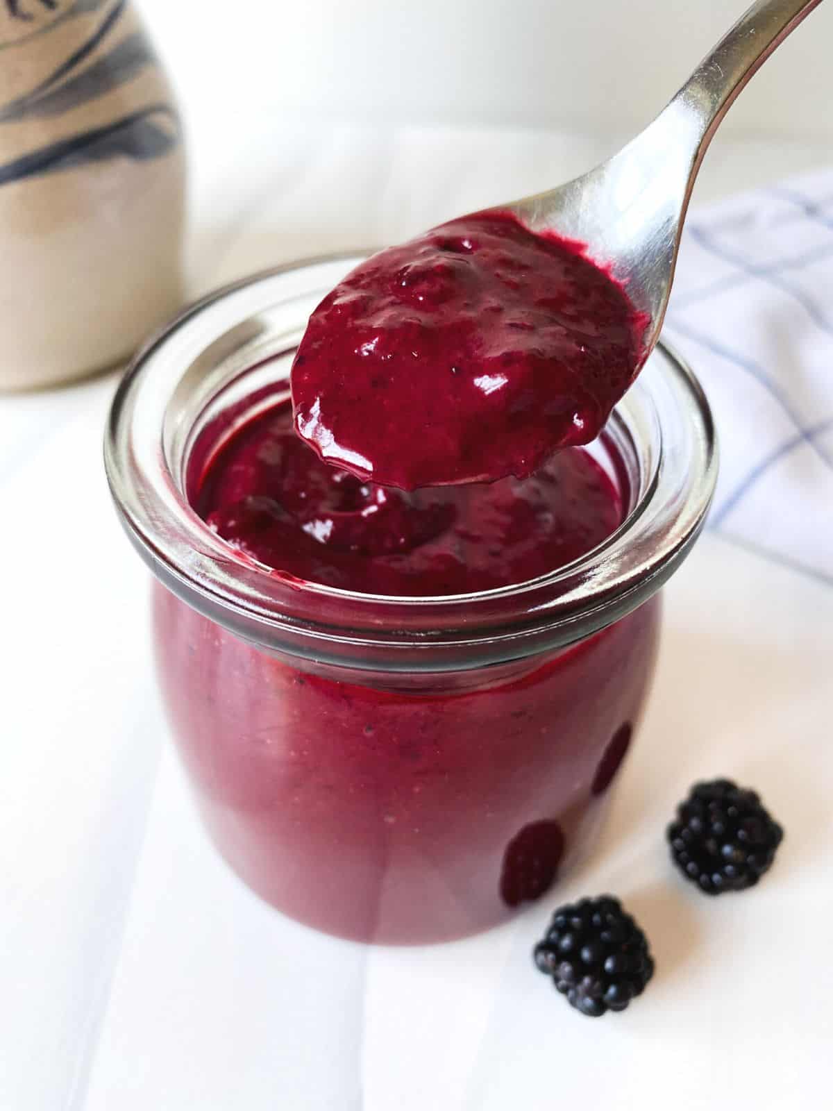 blackberry vinaigrette in a glass jar with a spoonful being held above it.