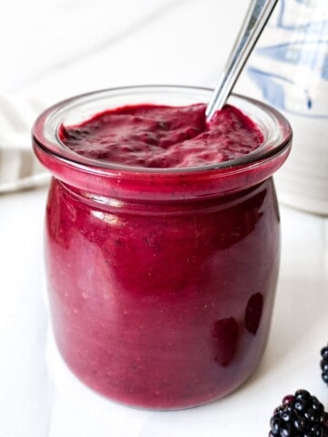 blackberry vinaigrette in a glass jar with a spoon in it next to blackberries.