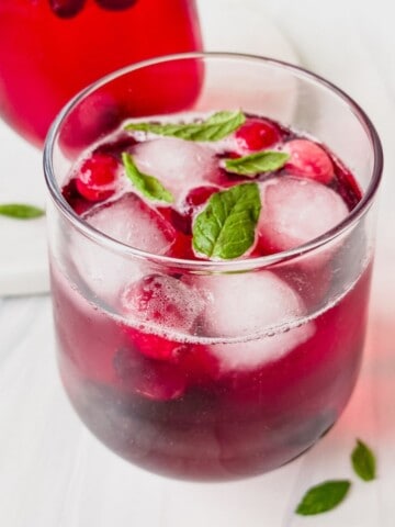 blackcurrant mocktail in a glass with mint and another glass in the background.