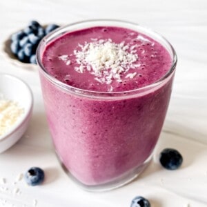 cherry blueberry smoothie in a glass with a bowl of blueberries in the background.