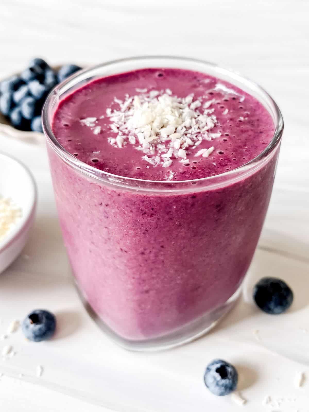 cherry blueberry smoothie in a glass sprinkled with coconut with a bowl of blueberries behind it.
