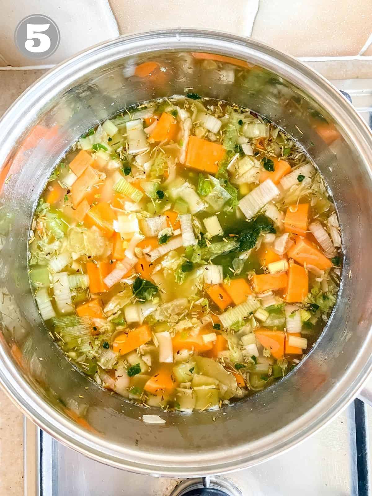 vegetables in chicken stock in a large pot with number five in the corner.