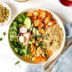 couscous buddha bowl next to a bowl of pistachios and cutlery on a blue cloth.