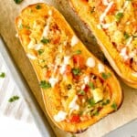 couscous stuffed butternut squash drizzled with tahini and herbs on a lined baking tray.
