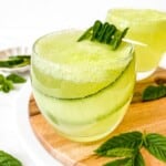 cucumber mint mocktail in a glass with a slice of cucumber in it on a wooden board with mint leaves.