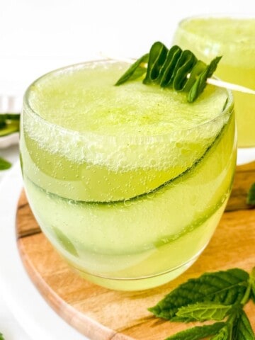 cucumber mint mocktail in a glass with a slice of cucumber in it on a wooden board with mint leaves.